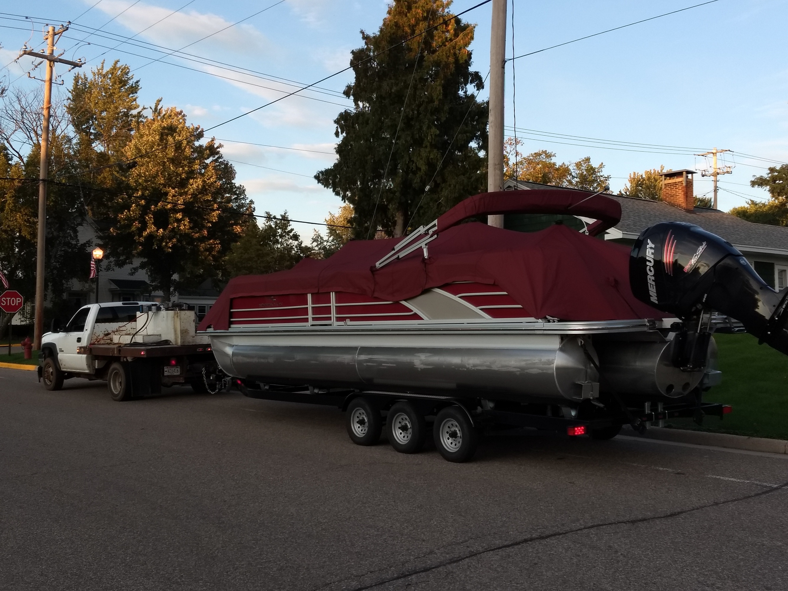 A tow truck hitched to a pontoon, parked on the street of a suburb.