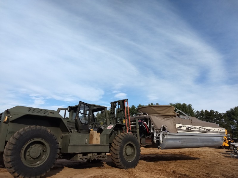 A military green tractor lifting a pontoon on a worksite.