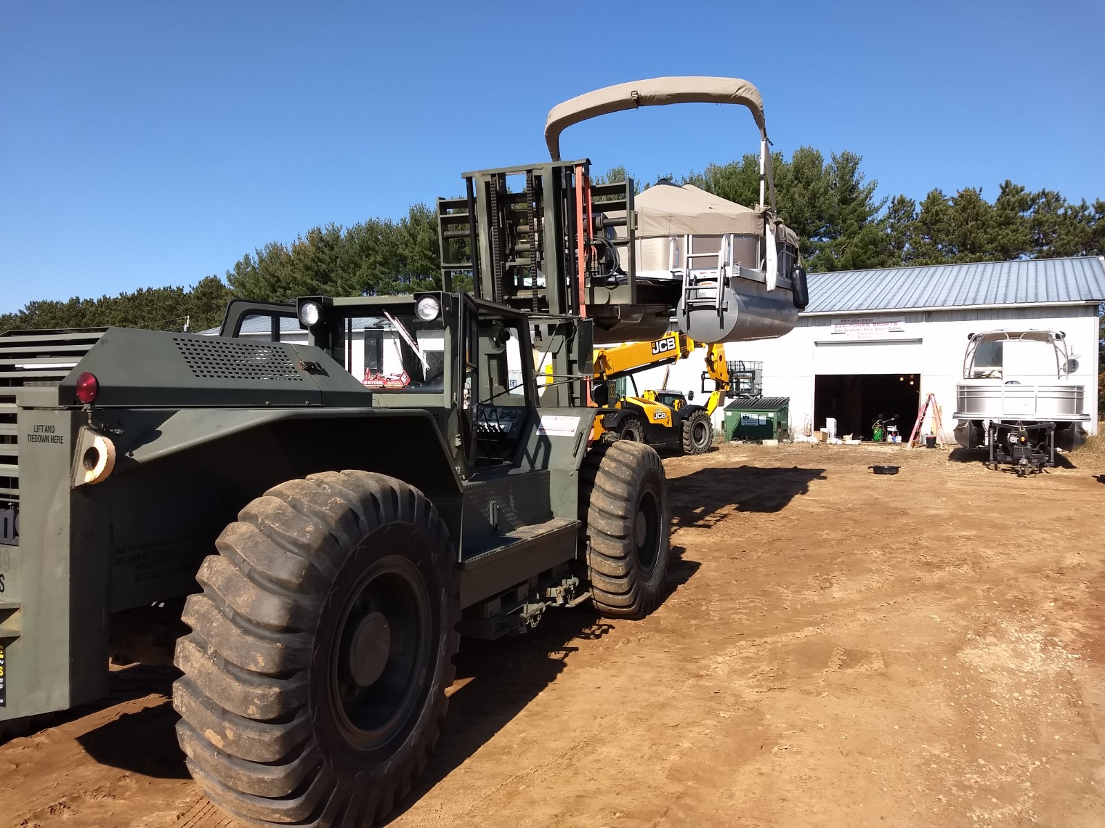 A large tractor lifting a pontoon in a sunny work area.