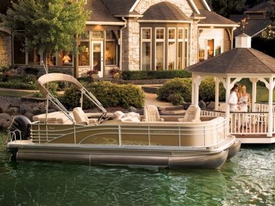 A Bennington pontoon afloat outside of a luxury house while a man and woman look out from the …